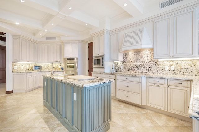 kitchen with custom exhaust hood, a center island with sink, light stone countertops, beam ceiling, and stainless steel appliances