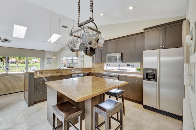 kitchen featuring kitchen peninsula, light stone counters, vaulted ceiling with skylight, a breakfast bar, and stainless steel appliances