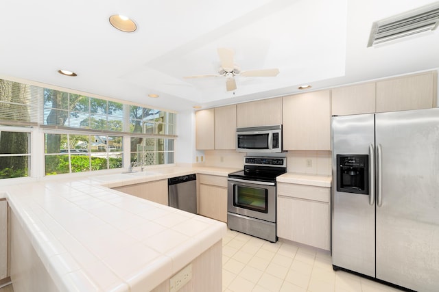 kitchen with light tile patterned floors, appliances with stainless steel finishes, tasteful backsplash, tile counters, and light brown cabinetry