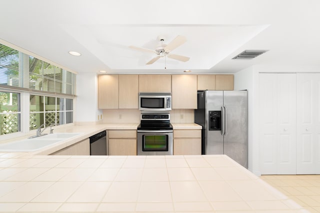 kitchen featuring stainless steel appliances, sink, light brown cabinetry, and a tray ceiling