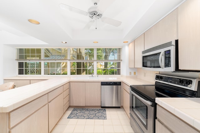 kitchen featuring light tile patterned flooring, appliances with stainless steel finishes, tile counters, and light brown cabinetry