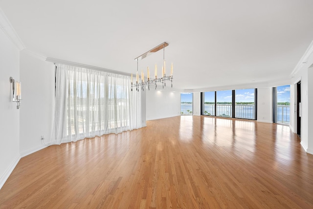 unfurnished living room featuring a chandelier, baseboards, ornamental molding, light wood-type flooring, and expansive windows