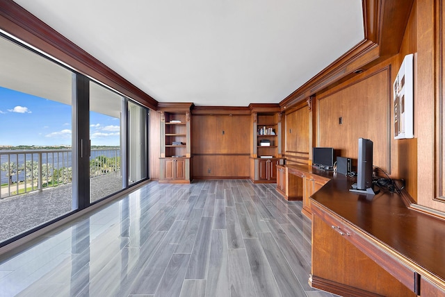 unfurnished office featuring wood walls, a water view, light wood-style floors, built in study area, and crown molding