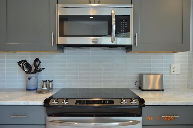 kitchen with gray cabinets, light stone countertops, and stainless steel appliances