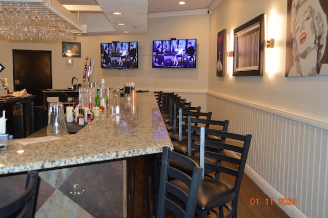 bar with crown molding, light stone counters, and dark hardwood / wood-style flooring