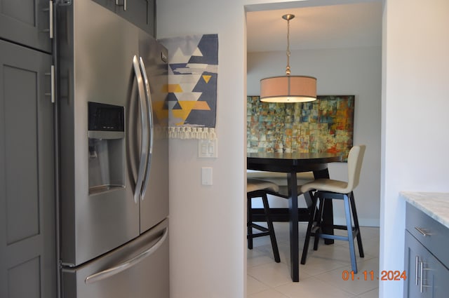 kitchen with light stone countertops, light tile patterned floors, pendant lighting, and stainless steel fridge