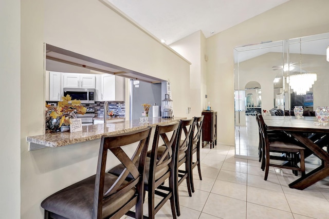 kitchen with light stone countertops, stainless steel appliances, tasteful backsplash, vaulted ceiling, and white cabinets