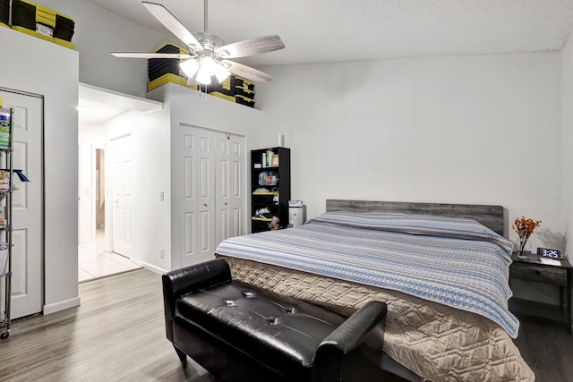 bedroom featuring high vaulted ceiling, ceiling fan, light wood-type flooring, a textured ceiling, and a closet