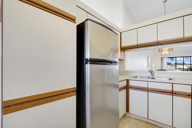 kitchen with sink, an inviting chandelier, light tile patterned floors, stainless steel fridge, and white cabinets