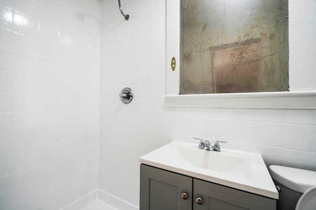 bathroom with tile walls, vanity, toilet, and tiled shower