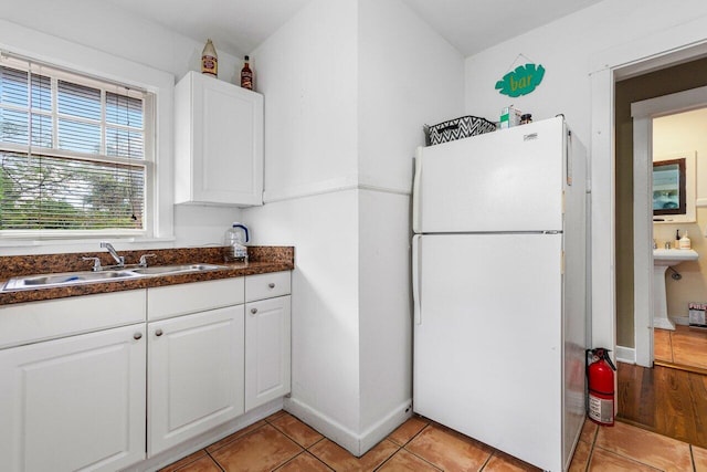 kitchen featuring white cabinets, light tile patterned floors, white fridge, and sink