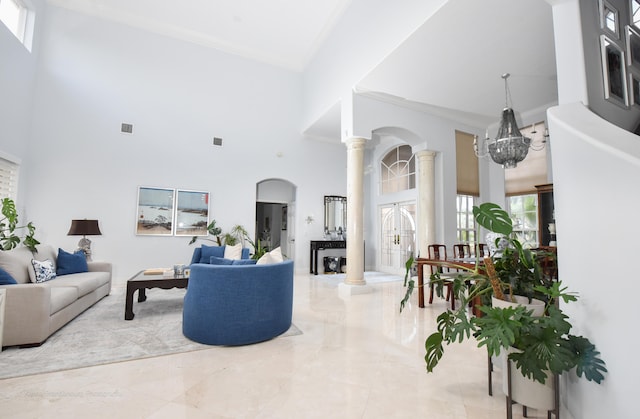 living room featuring ornate columns, a notable chandelier, a high ceiling, and crown molding