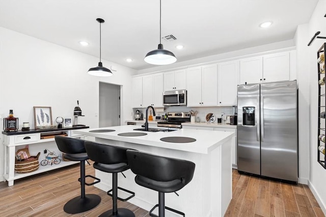 kitchen featuring white cabinetry, light hardwood / wood-style floors, appliances with stainless steel finishes, and a kitchen island with sink