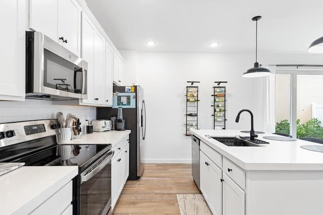 kitchen with an island with sink, stainless steel appliances, pendant lighting, light wood-type flooring, and white cabinetry