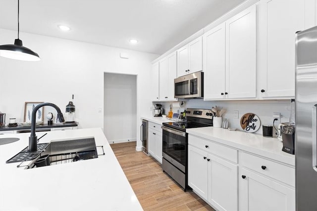 kitchen featuring appliances with stainless steel finishes, light hardwood / wood-style flooring, white cabinets, and hanging light fixtures