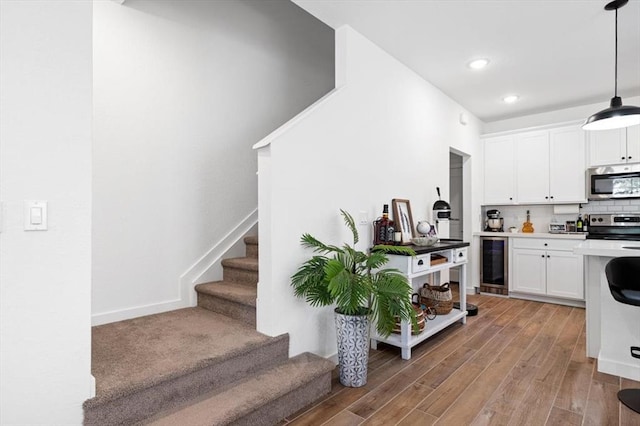 kitchen with appliances with stainless steel finishes, light wood-type flooring, pendant lighting, white cabinets, and wine cooler