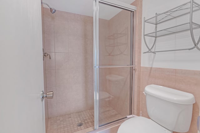 bathroom featuring a shower with door, toilet, and tile walls