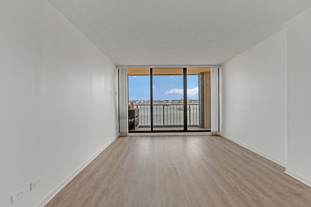 empty room with light hardwood / wood-style flooring, a wall of windows, and a textured ceiling