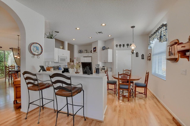 kitchen with white cabinets, light wood-type flooring, kitchen peninsula, and plenty of natural light