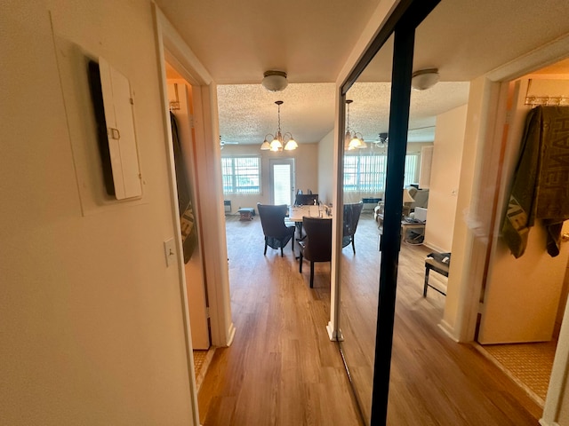 hallway featuring electric panel, light hardwood / wood-style flooring, a notable chandelier, and a textured ceiling