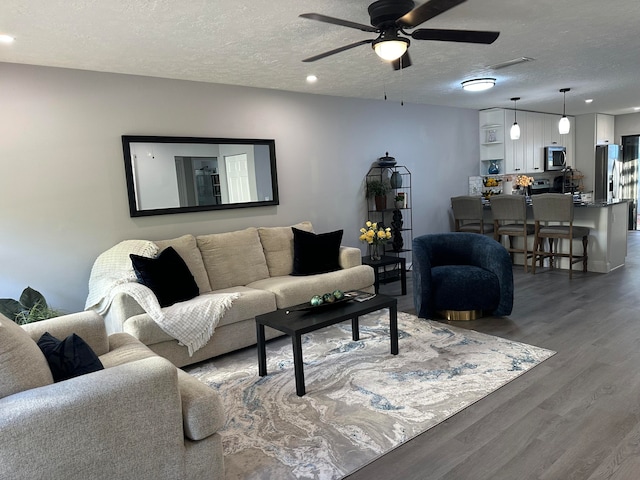 living room featuring ceiling fan, dark hardwood / wood-style flooring, and a textured ceiling