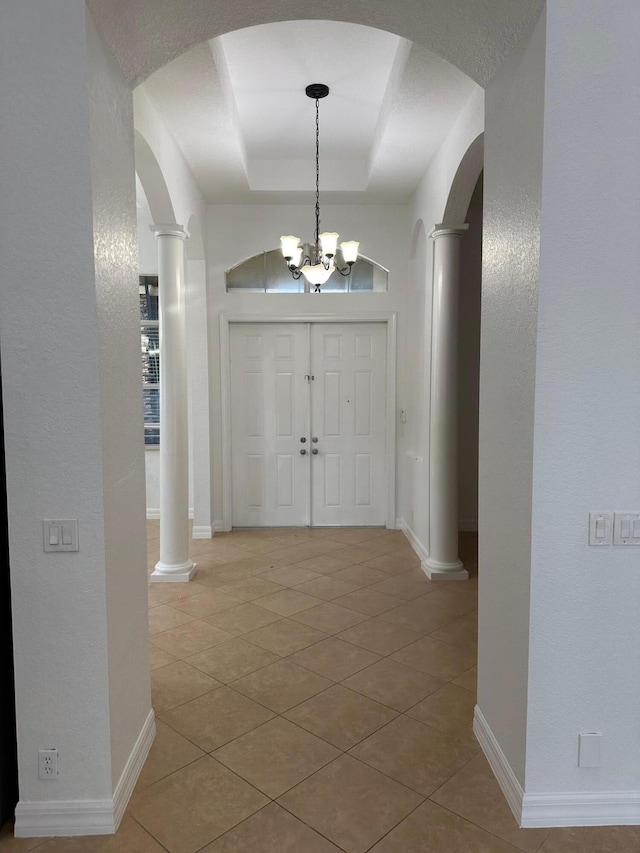 foyer with a tray ceiling, tile patterned floors, decorative columns, and a notable chandelier