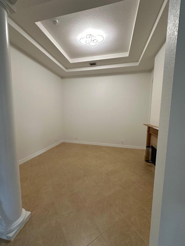 tiled empty room featuring a raised ceiling and a textured ceiling