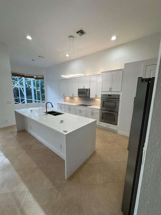 kitchen featuring appliances with stainless steel finishes, sink, decorative light fixtures, white cabinetry, and an island with sink