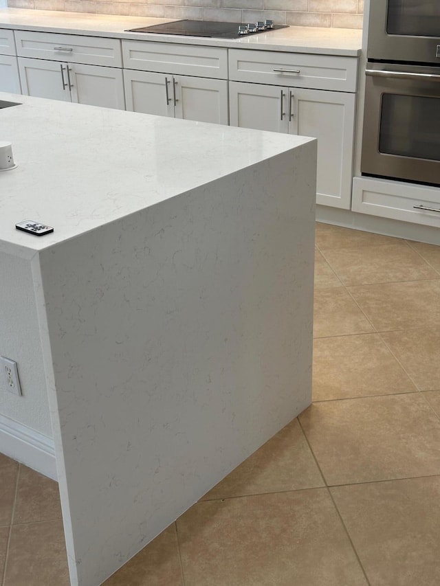 kitchen with white cabinets, decorative backsplash, black electric stovetop, and light tile patterned floors