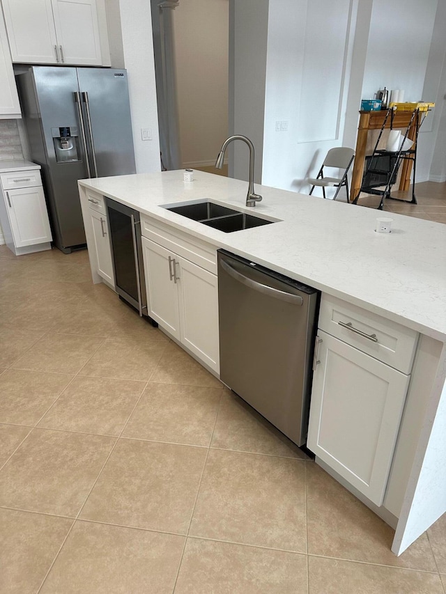 kitchen with appliances with stainless steel finishes, light stone counters, sink, white cabinetry, and light tile patterned flooring