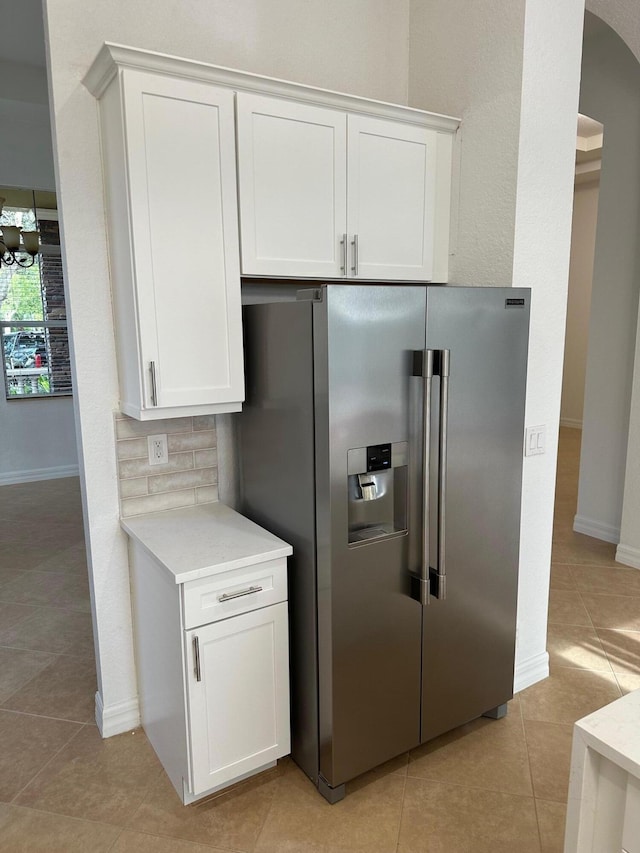 kitchen featuring light stone countertops, light tile patterned floors, backsplash, high quality fridge, and white cabinets