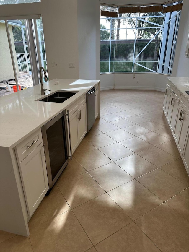 kitchen with sink, stainless steel dishwasher, light tile patterned flooring, white cabinetry, and beverage cooler