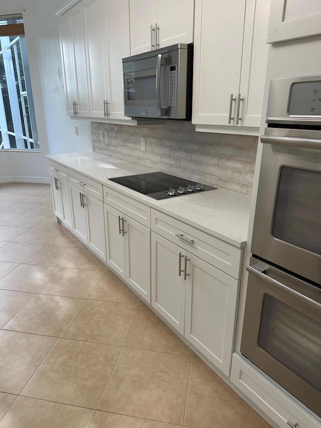 kitchen featuring light stone countertops, white cabinetry, stainless steel appliances, tasteful backsplash, and light tile patterned flooring