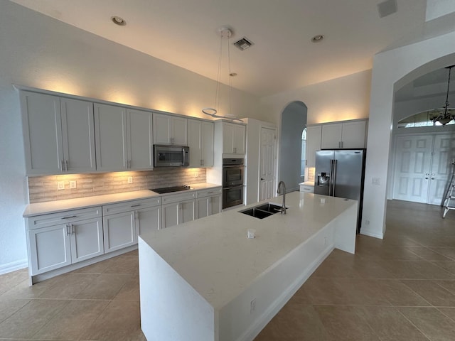 kitchen with sink, decorative light fixtures, a center island with sink, light tile patterned floors, and appliances with stainless steel finishes