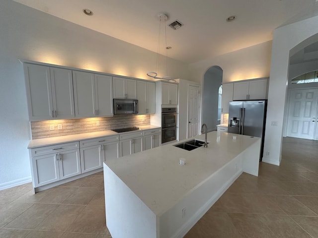 kitchen with a center island with sink, sink, tasteful backsplash, decorative light fixtures, and stainless steel appliances