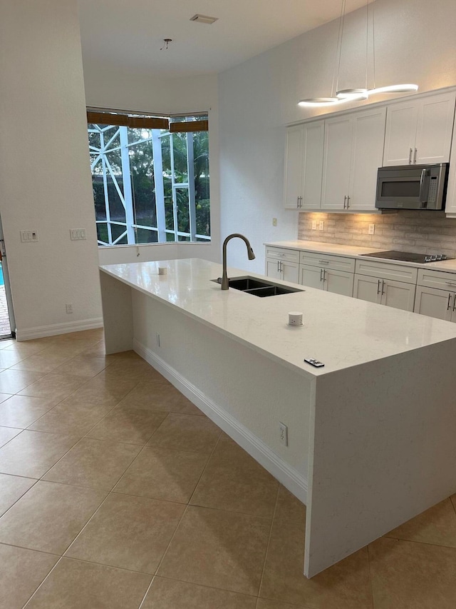 kitchen with light stone countertops, sink, hanging light fixtures, and a center island with sink