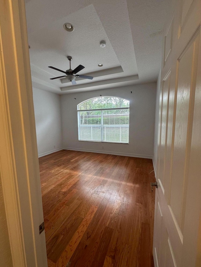 empty room featuring ceiling fan, a raised ceiling, and wood-type flooring