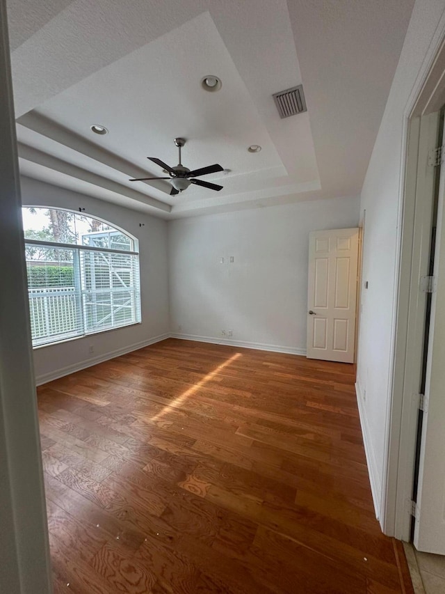 empty room featuring a raised ceiling, ceiling fan, and hardwood / wood-style floors