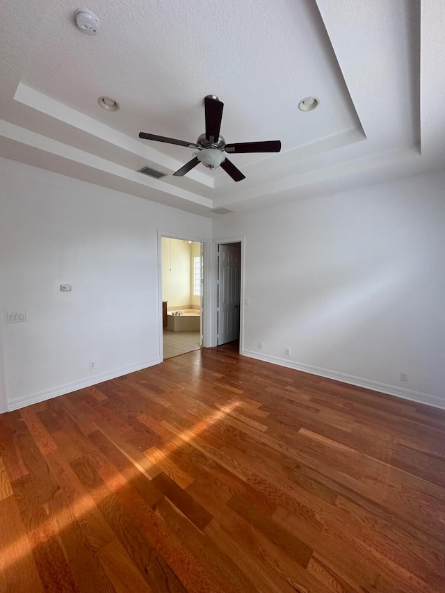 unfurnished bedroom with a tray ceiling, ceiling fan, wood-type flooring, and a textured ceiling