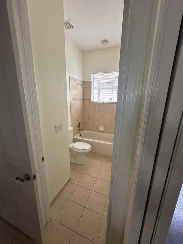 bathroom featuring tile patterned flooring, tiled shower / bath combo, and toilet