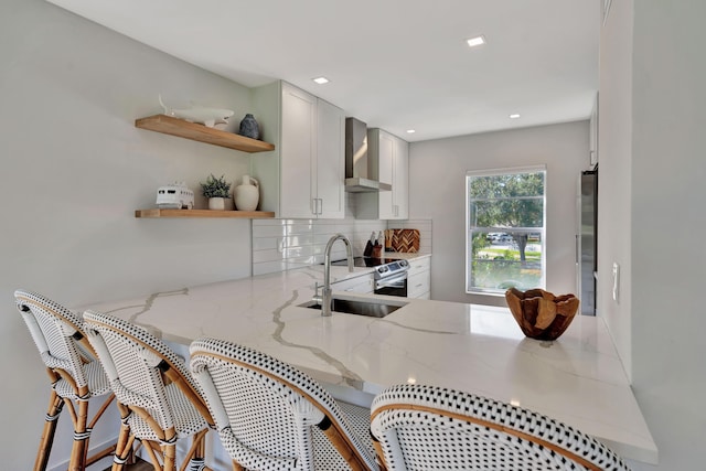 kitchen featuring white cabinets, light stone counters, wall chimney exhaust hood, and sink