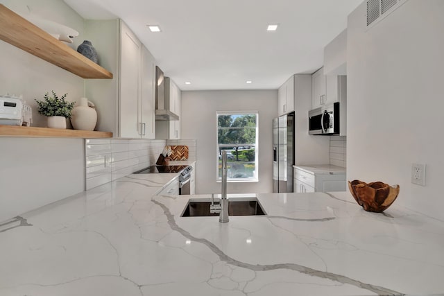 kitchen featuring light stone countertops, appliances with stainless steel finishes, wall chimney range hood, sink, and white cabinets