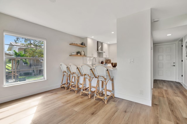 kitchen featuring wall chimney exhaust hood, light hardwood / wood-style floors, and white cabinetry