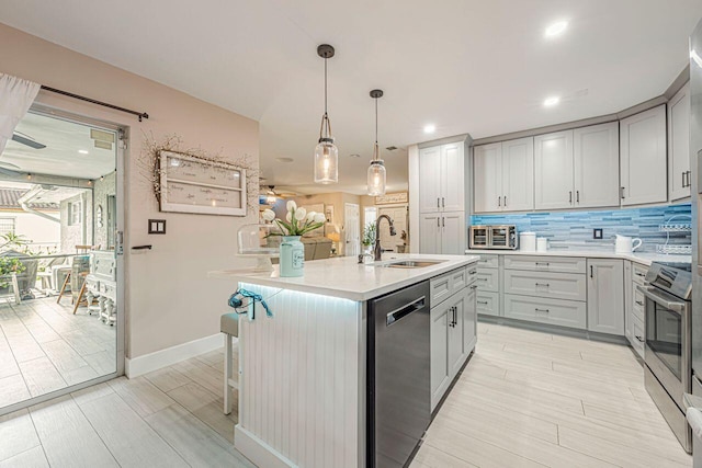 kitchen featuring gray cabinetry, appliances with stainless steel finishes, hanging light fixtures, sink, and an island with sink