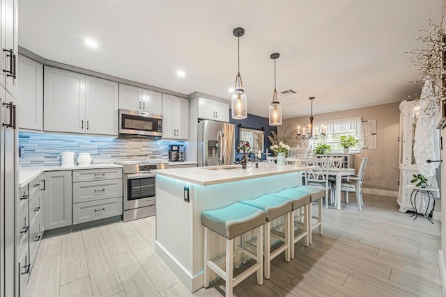 kitchen with stainless steel appliances, a kitchen breakfast bar, decorative light fixtures, a kitchen island with sink, and gray cabinetry