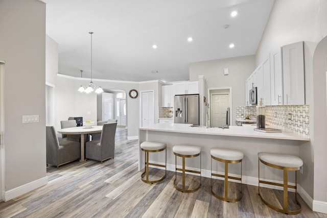 kitchen with stainless steel appliances, kitchen peninsula, hanging light fixtures, white cabinetry, and light hardwood / wood-style flooring