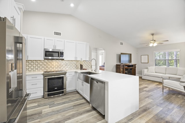 kitchen with appliances with stainless steel finishes, sink, white cabinets, kitchen peninsula, and light hardwood / wood-style flooring