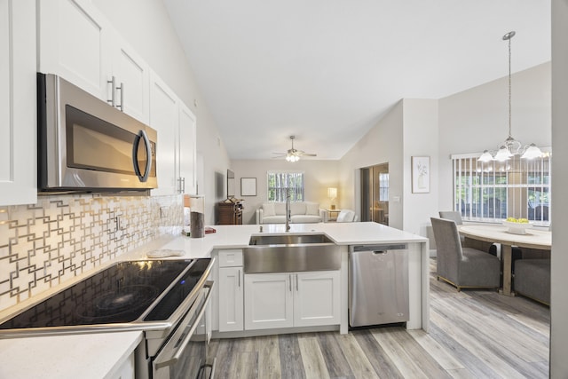 kitchen with lofted ceiling, hanging light fixtures, sink, white cabinetry, and appliances with stainless steel finishes