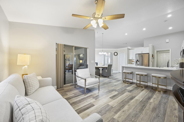 living room with ceiling fan with notable chandelier, light hardwood / wood-style flooring, and lofted ceiling