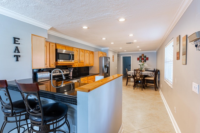 kitchen featuring stainless steel appliances, ornamental molding, light tile patterned floors, and a breakfast bar area